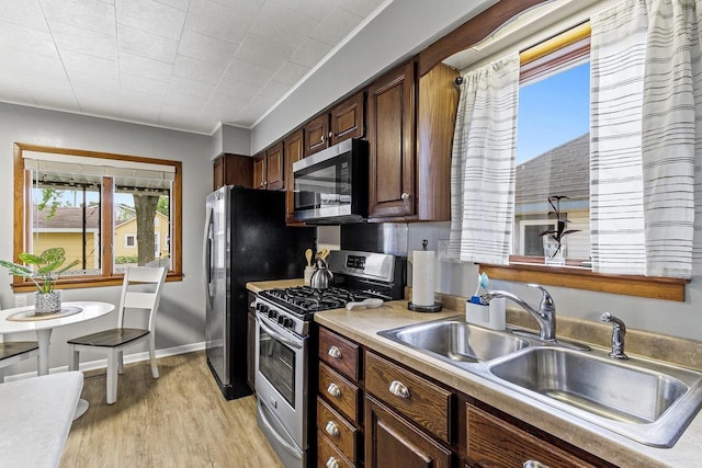 kitchen with light wood-style flooring, a sink, stainless steel appliances, light countertops, and baseboards