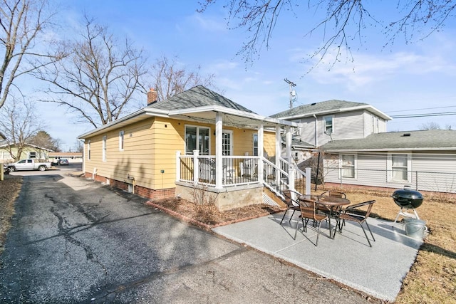 rear view of house with covered porch, driveway, a chimney, and a patio