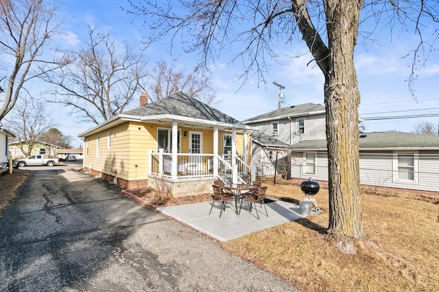 back of property featuring a porch, a chimney, driveway, and a shingled roof