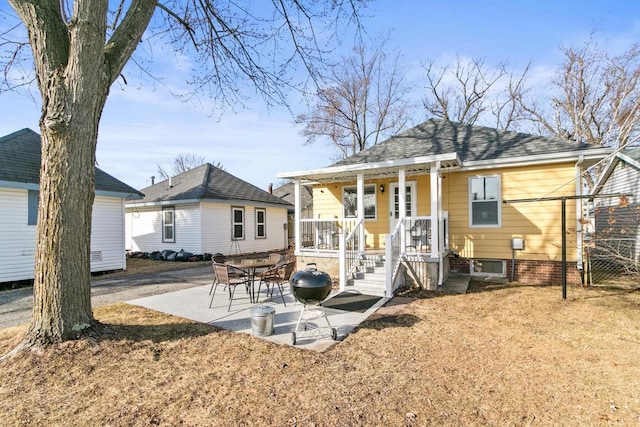 back of house with covered porch, a shingled roof, and a patio area