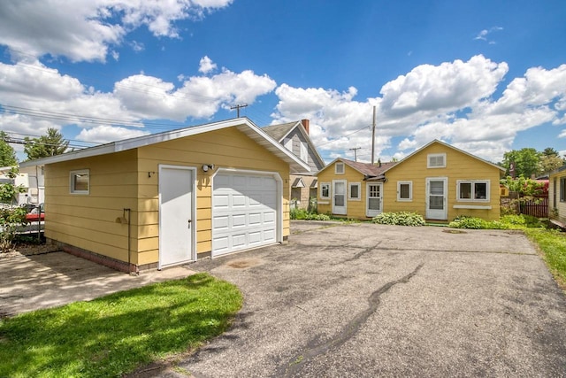 exterior space featuring an outbuilding, aphalt driveway, a detached garage, and fence