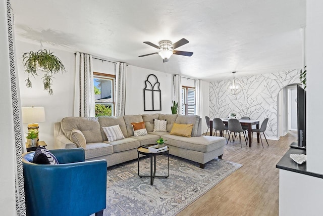 living room with light wood-type flooring, ceiling fan with notable chandelier, an accent wall, and wallpapered walls