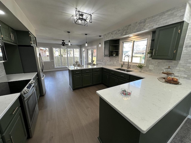 kitchen featuring a sink, dark wood finished floors, a peninsula, appliances with stainless steel finishes, and decorative backsplash