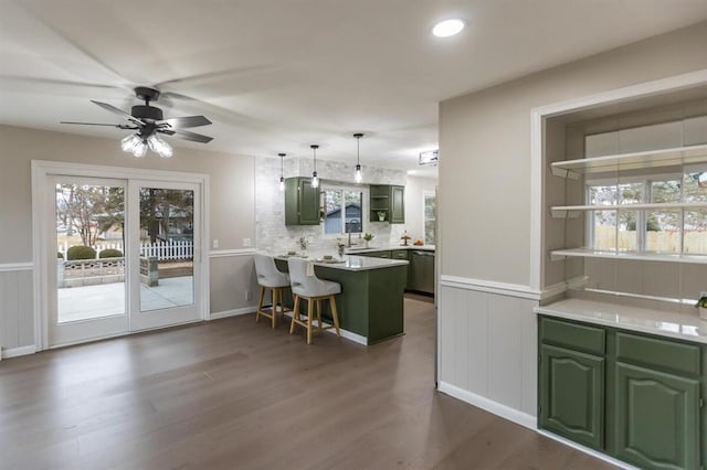 kitchen with green cabinets, a peninsula, dark wood finished floors, and wainscoting