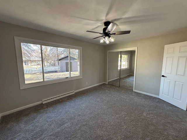 unfurnished bedroom featuring a baseboard heating unit, baseboards, a closet, a ceiling fan, and dark colored carpet