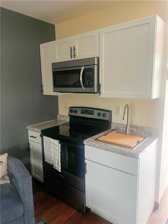 kitchen featuring stainless steel microwave, range with electric stovetop, light countertops, and white cabinetry