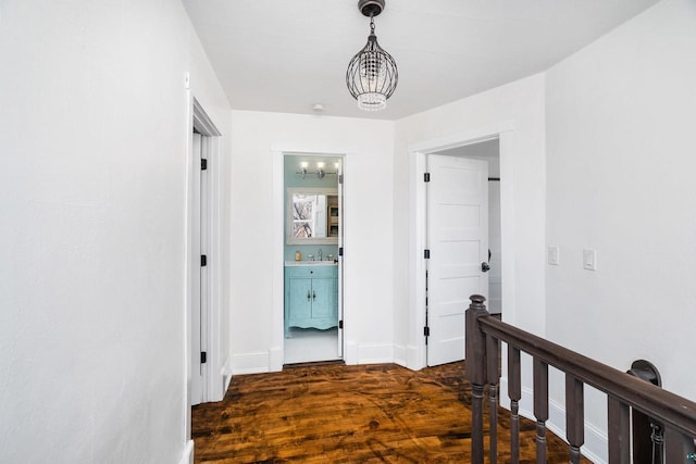 corridor featuring wood finished floors, an upstairs landing, baseboards, and a chandelier