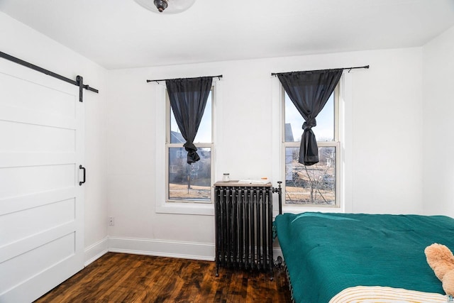 bedroom featuring a barn door, baseboards, radiator, and dark wood-style flooring