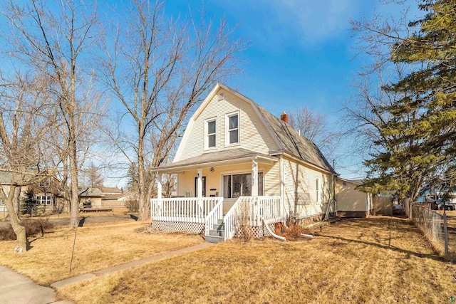 colonial inspired home with covered porch, a gambrel roof, a front yard, and fence