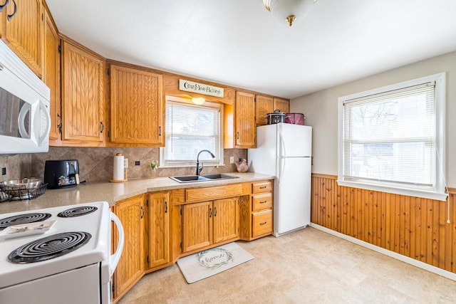 kitchen with white appliances, light countertops, a wainscoted wall, and a sink