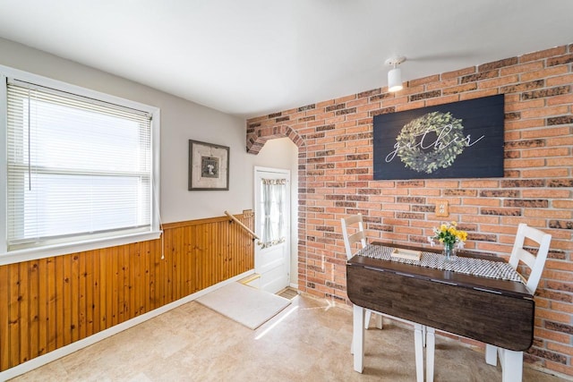 dining space featuring wooden walls, arched walkways, brick wall, and wainscoting