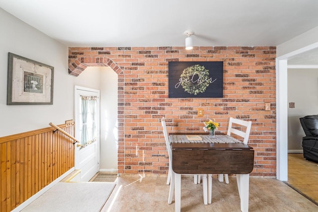 dining space with a wainscoted wall, wood walls, and brick wall