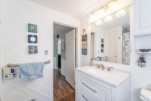 full bathroom featuring a textured ceiling, wood finished floors, vanity, and toilet