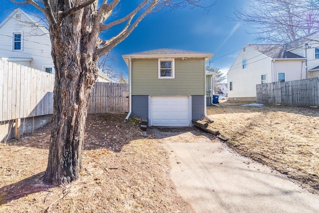 rear view of property featuring concrete driveway, an attached garage, and fence