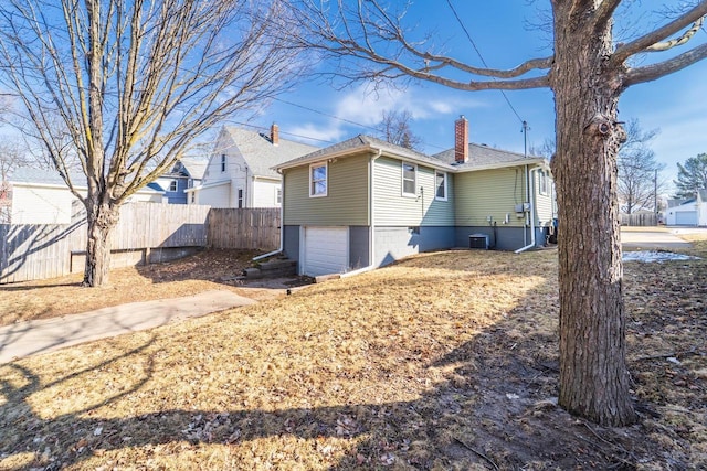 view of property exterior featuring an attached garage, a chimney, and fence