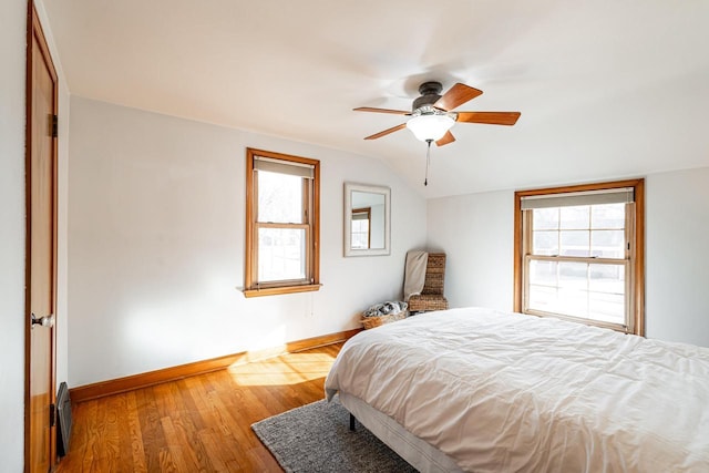 bedroom featuring multiple windows, lofted ceiling, baseboards, and wood finished floors