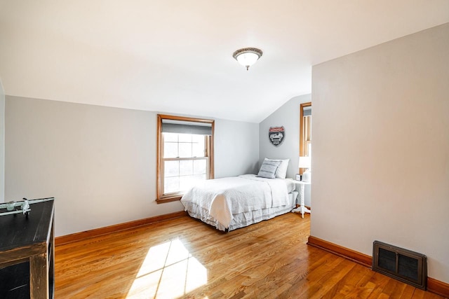 bedroom featuring vaulted ceiling, visible vents, baseboards, and wood finished floors