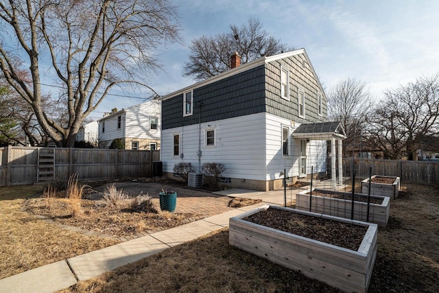 rear view of house featuring a fenced backyard, a patio area, a chimney, and a vegetable garden