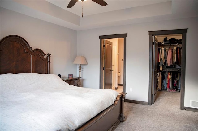 bedroom with a walk in closet, light carpet, a raised ceiling, a closet, and baseboards