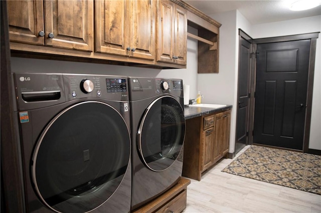 laundry area featuring a sink, cabinet space, separate washer and dryer, and light wood-style flooring