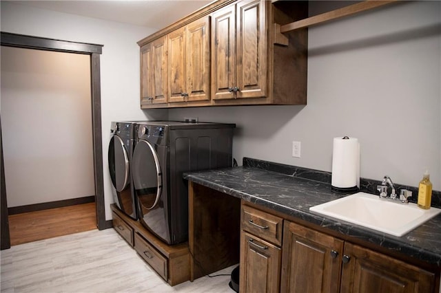 clothes washing area with a sink, cabinet space, light wood-style floors, baseboards, and washing machine and clothes dryer