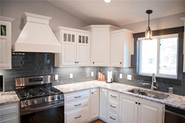 kitchen featuring premium range hood, stainless steel range with gas stovetop, a sink, white cabinets, and dishwasher