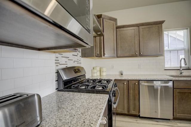 kitchen with decorative backsplash, light stone counters, appliances with stainless steel finishes, and a sink