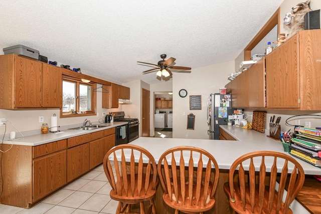 kitchen featuring independent washer and dryer, a sink, freestanding refrigerator, gas stove, and light countertops