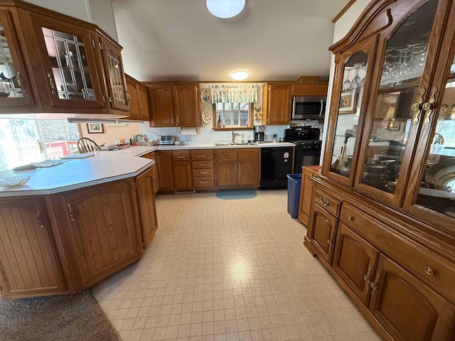 kitchen featuring brown cabinets, black appliances, a sink, glass insert cabinets, and light floors