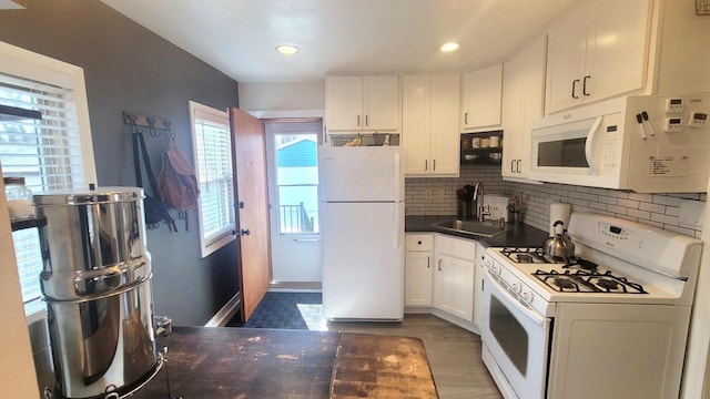 kitchen with dark countertops, tasteful backsplash, white cabinets, white appliances, and a sink