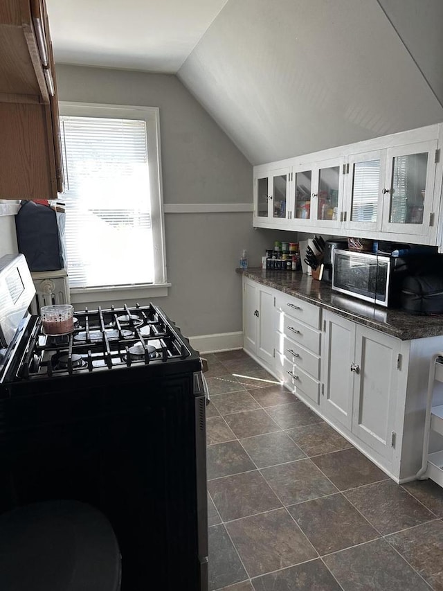 kitchen featuring glass insert cabinets, baseboards, lofted ceiling, appliances with stainless steel finishes, and white cabinetry