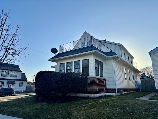 view of side of home with a yard, a balcony, and fence