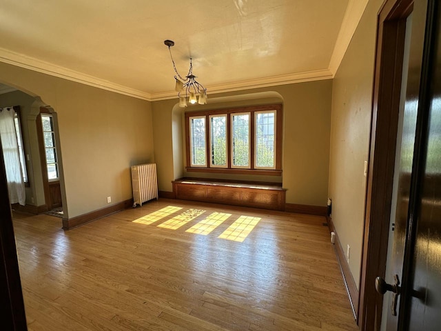 empty room with arched walkways, wood finished floors, radiator heating unit, and ornamental molding