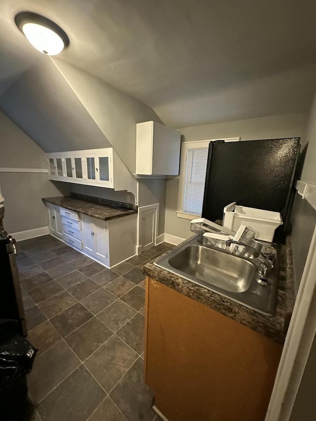 kitchen featuring dark tile patterned flooring, a sink, dark countertops, white cabinetry, and lofted ceiling