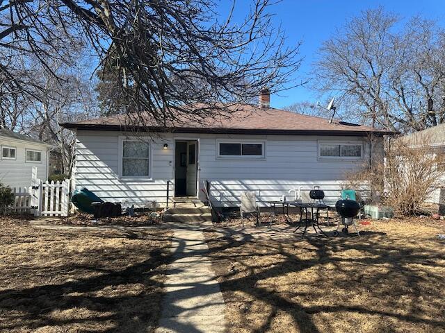 back of property with entry steps, roof with shingles, a chimney, and fence