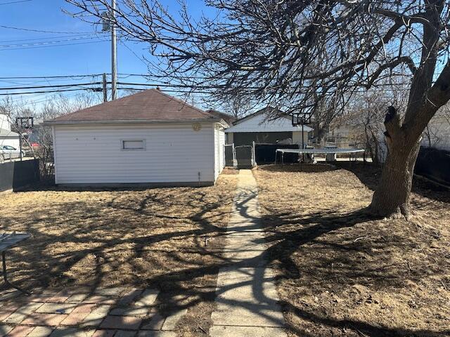 exterior space with a trampoline, roof with shingles, an outdoor structure, and fence