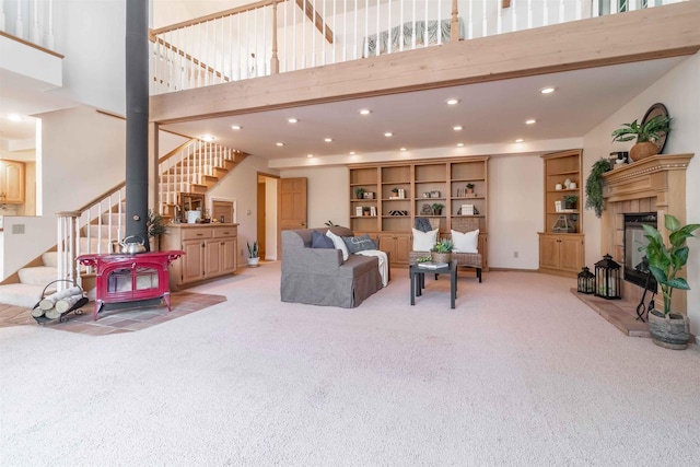 living room with stairway, recessed lighting, a towering ceiling, a glass covered fireplace, and light colored carpet