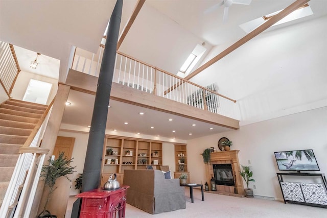 living room with high vaulted ceiling, a skylight, a tile fireplace, and carpet