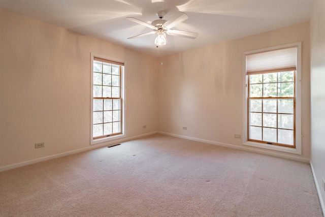 carpeted spare room featuring baseboards, visible vents, and ceiling fan