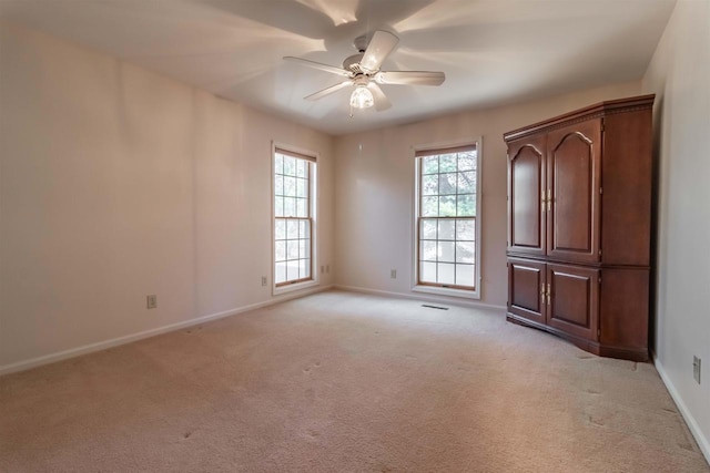 empty room with visible vents, baseboards, light colored carpet, and ceiling fan