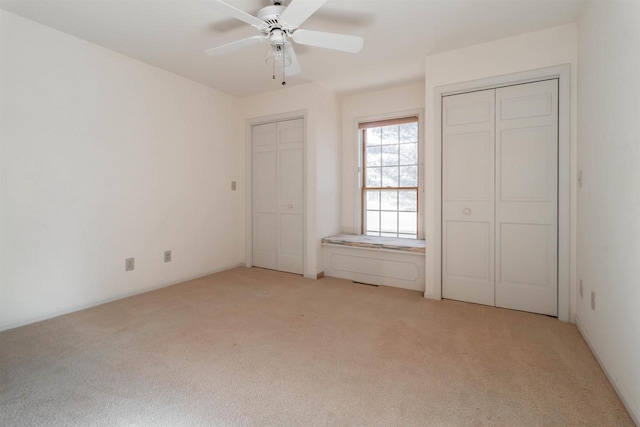 unfurnished bedroom featuring light carpet, two closets, and a ceiling fan