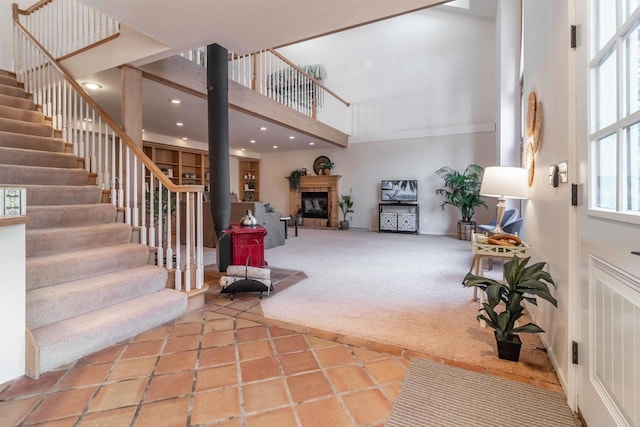 interior space featuring stairway, carpet floors, recessed lighting, a towering ceiling, and a glass covered fireplace