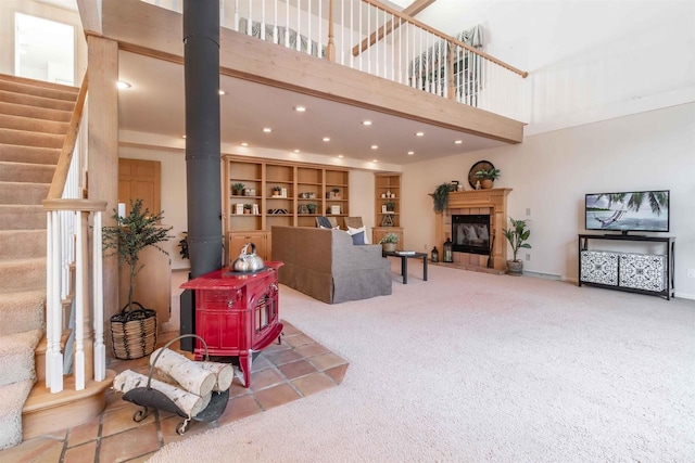 living room with a wood stove, a tiled fireplace, carpet, a towering ceiling, and stairs