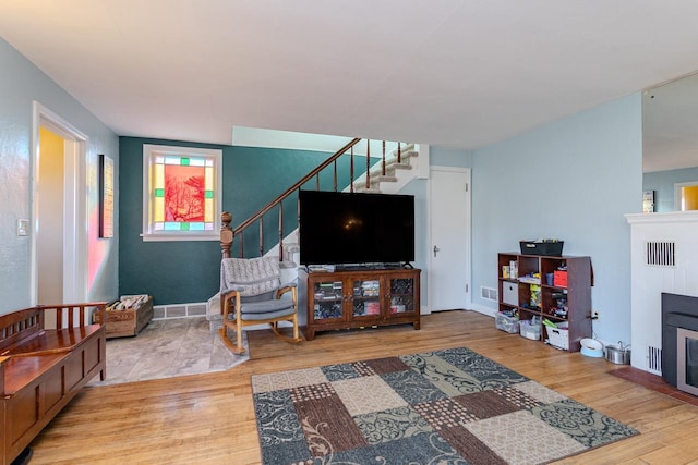 living room with a glass covered fireplace, stairway, wood finished floors, and visible vents