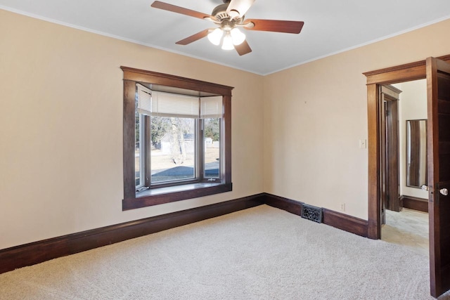 carpeted empty room with crown molding, a ceiling fan, and baseboards