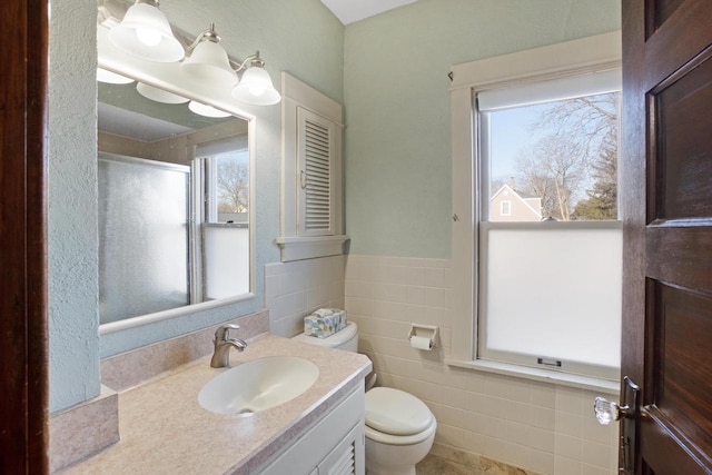 bathroom featuring a shower with shower door, toilet, tile walls, wainscoting, and vanity