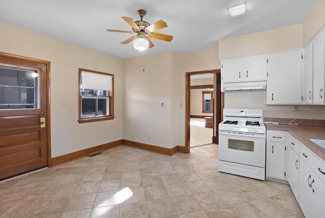 kitchen featuring under cabinet range hood, baseboards, white gas stove, and white cabinets