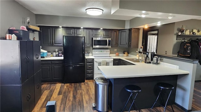 kitchen with stainless steel microwave, a peninsula, freestanding refrigerator, white electric range, and a sink