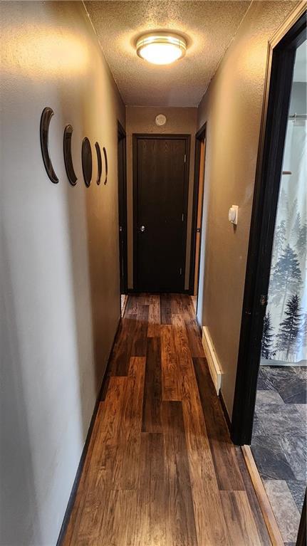 hall with baseboards, a textured ceiling, and dark wood-style flooring