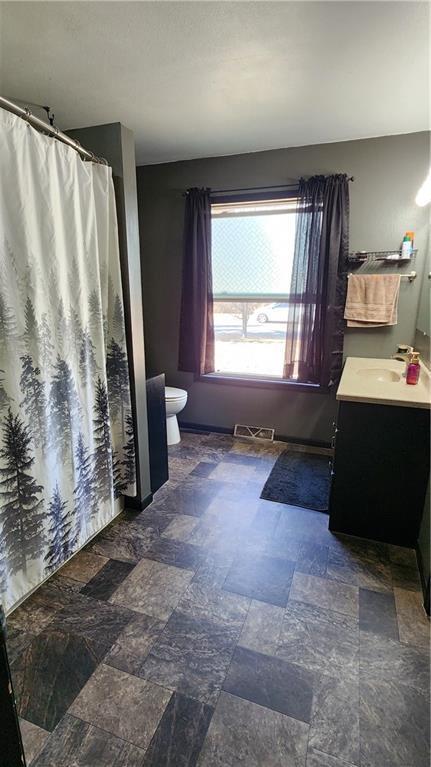 full bath with visible vents, stone finish flooring, toilet, a shower with shower curtain, and vanity